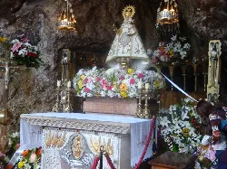Statue of the Virgin of Covadonga in a grotto with flowers and religious decorations.