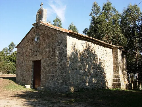 Pequeña iglesia de piedra con tejado de tejas y cruz en la parte superior en Culleredo.