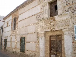 Fachada de una casa antigua con ventanas con rejas y detalles en piedra.
