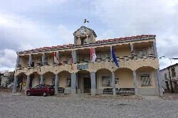 Navasfrías town hall building with flags and a clock on the central tower.