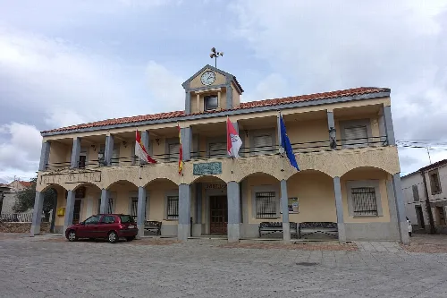 Navasfrías town hall building with flags and a clock on the central tower.