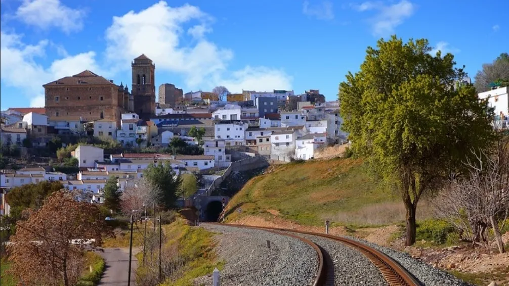 Vías de tren en primer plano y pueblo con iglesia en la colina al fondo.