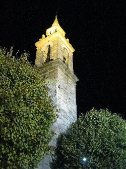Church tower with bell and pointed roof, surrounded by greenery.