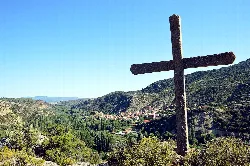 Gran cruz de piedra en primer plano con vista de El Cuervo y montañas en el fondo.