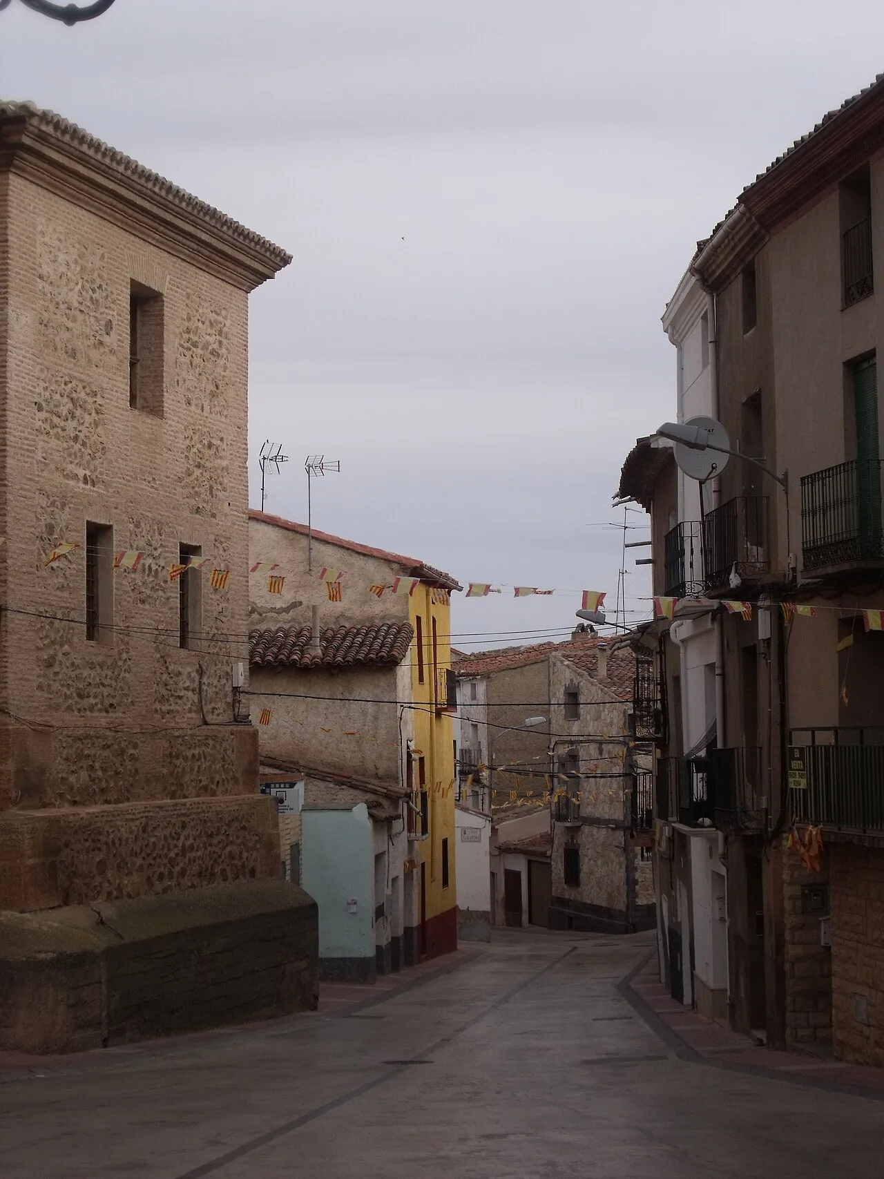 Calle de Aguarón con casas de piedra y balcones, bajo un cielo nublado.