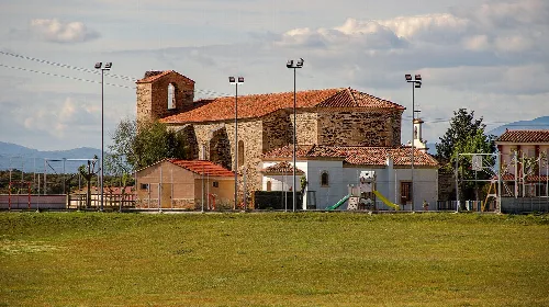 Steinbau mit Glockenturm neben Spielplatz und offenem Feld.
