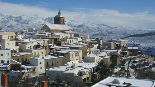 Casas blancas en una colina con montañas nevadas en el fondo.