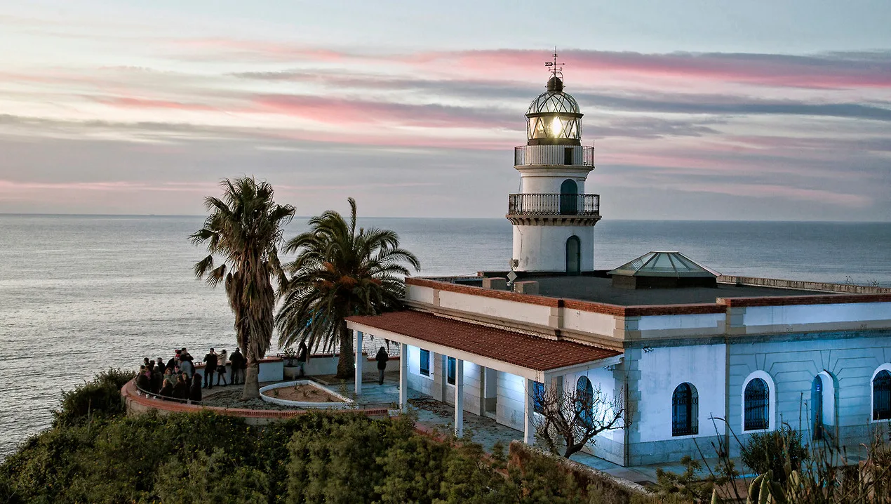 Leuchtturm aus dem 19. Jahrhundert in Calella mit Menschen und Palmen.