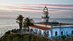 Leuchtturm aus dem 19. Jahrhundert in Calella mit Menschen und Palmen.