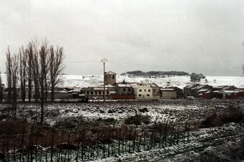 Pueblo con casas y iglesia en un paisaje nevado en Valladolid.