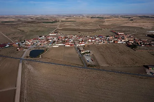 Luftaufnahme eines Dorfes mit Feldern und einem kleinen See in Ávila.