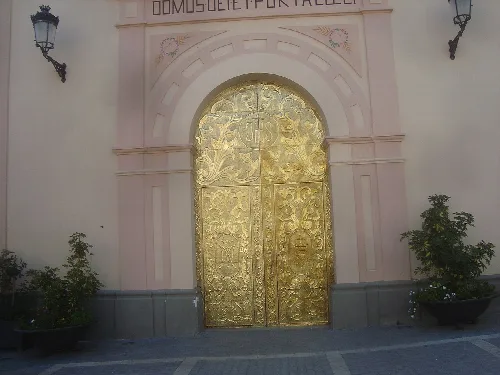 Puerta de la iglesia con detalles dorados y macetas a los lados.
