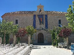 Stone church facade with trees and chairs in front.