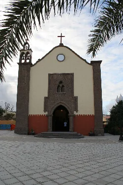 Facade of a church with cross at the top and palm trees on the sides.