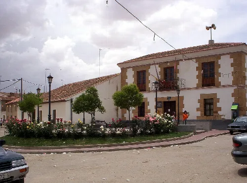 Platz mit Bäumen, Blumen und einem zweistöckigen Gebäude in Vadillo de la Guareña.