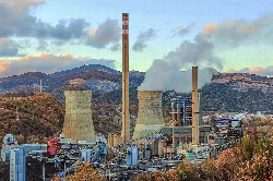 Central térmica con chimeneas y montañas en el fondo.