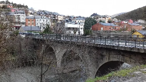 Brücke von Domingo Flórez über den Fluss Sil mit Häusern und Hügeln im Hintergrund.
