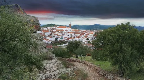 Blick auf Encinasola mit weißen Häusern, Festung und grünen Bäumen unter dunklem Himmel.