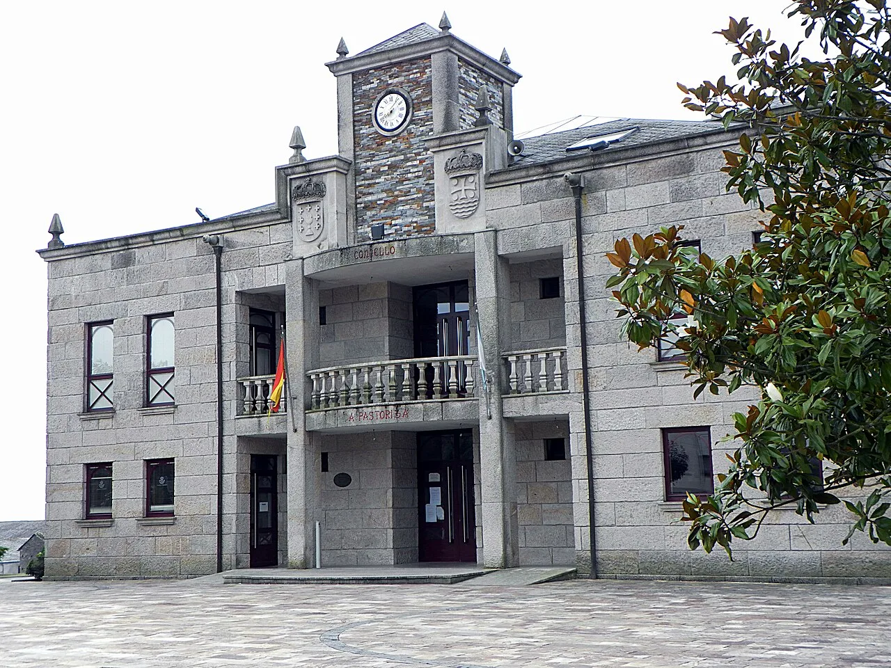 Stone town hall building with clock and coat of arms.