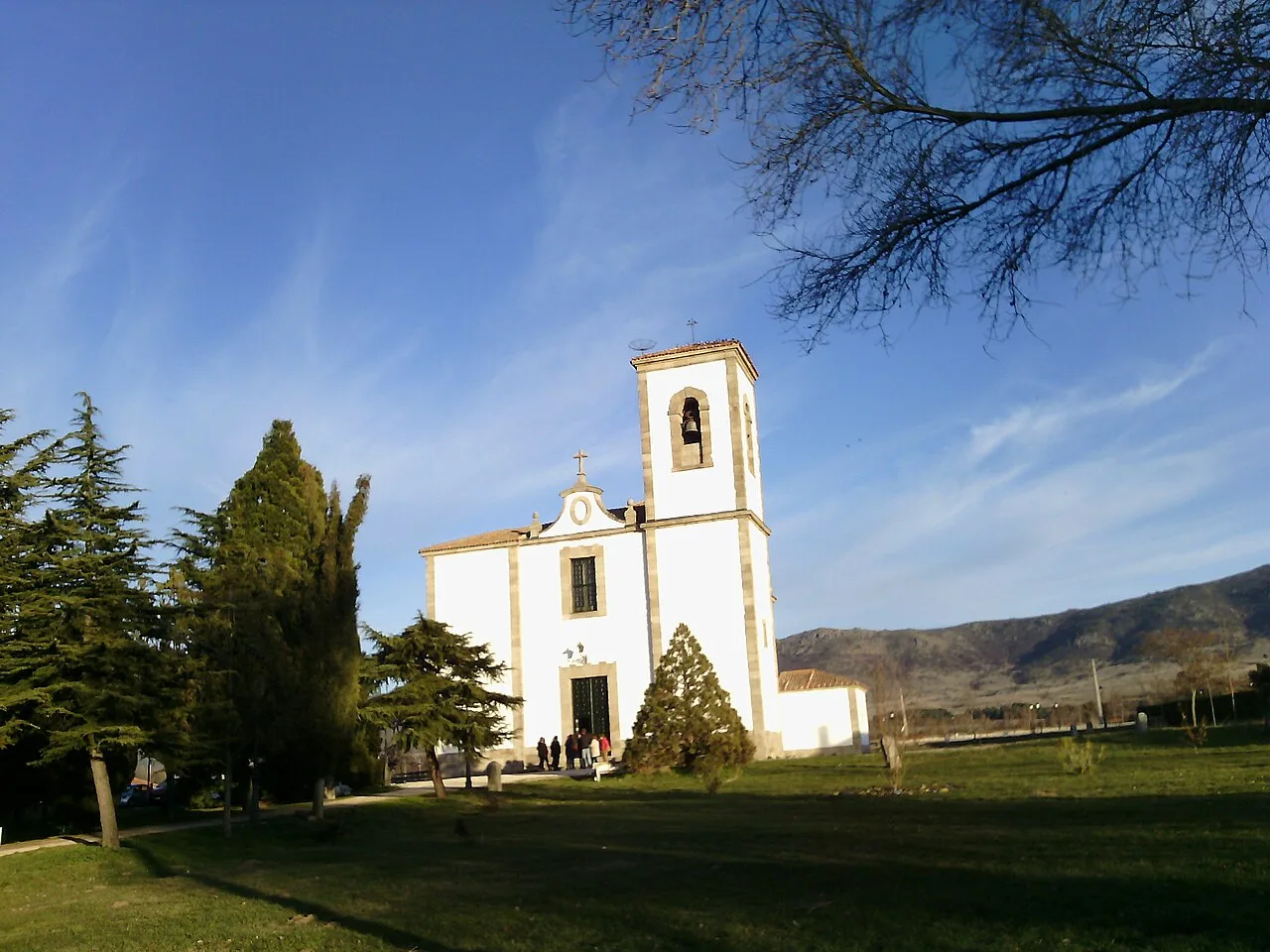Iglesia blanca con torre y árboles verdes frente a un cielo azul.