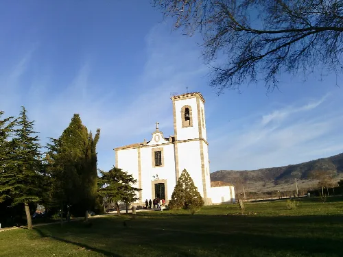 White church with tower and green trees against a blue sky.