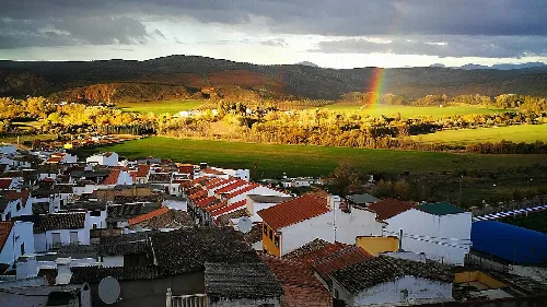 Blick auf Häuser mit roten und grünen Dächern, und einen Regenbogen am Himmel.