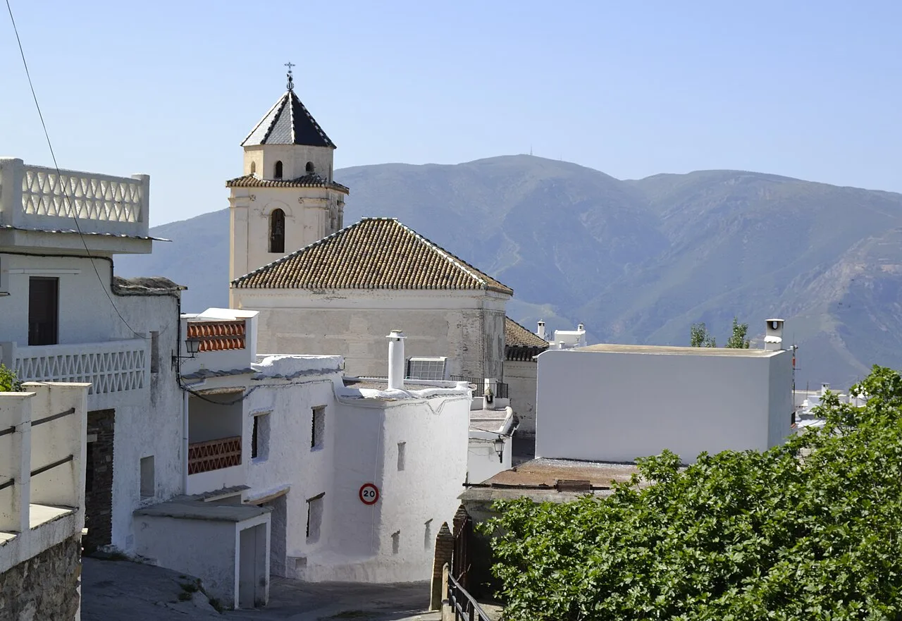 Weiße Häuser und eine Kirche in Cáñar mit Bergen im Hintergrund.