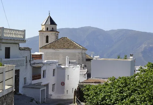 Weiße Häuser und eine Kirche in Cáñar mit Bergen im Hintergrund.