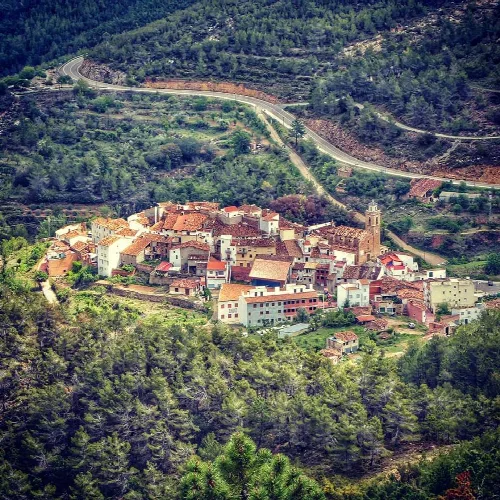 Vista panorámica de un pueblo en una zona montañosa con árboles y caminos.