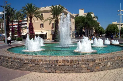 Fuente con varias cascadas en una plaza de Salou con palmeras y edificios.
