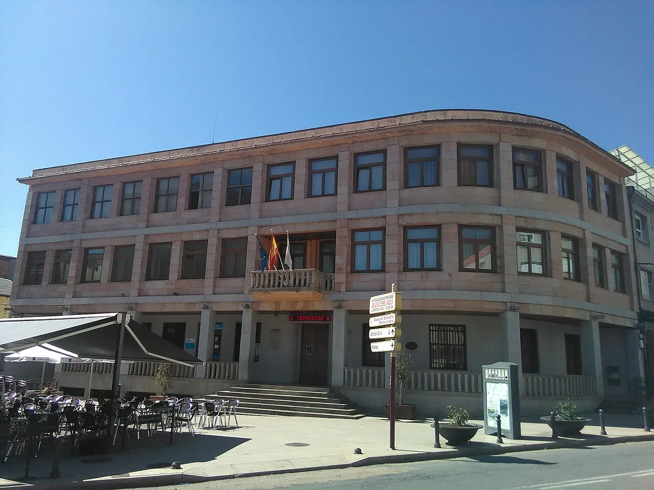 Edificio de forma rectangular con varias ventanas y bandera en la fachada.