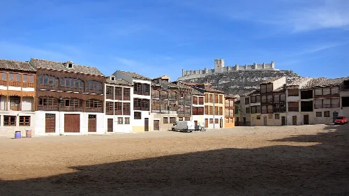 Plaza del Coso con edificios y castillo en el fondo, cielo azul.