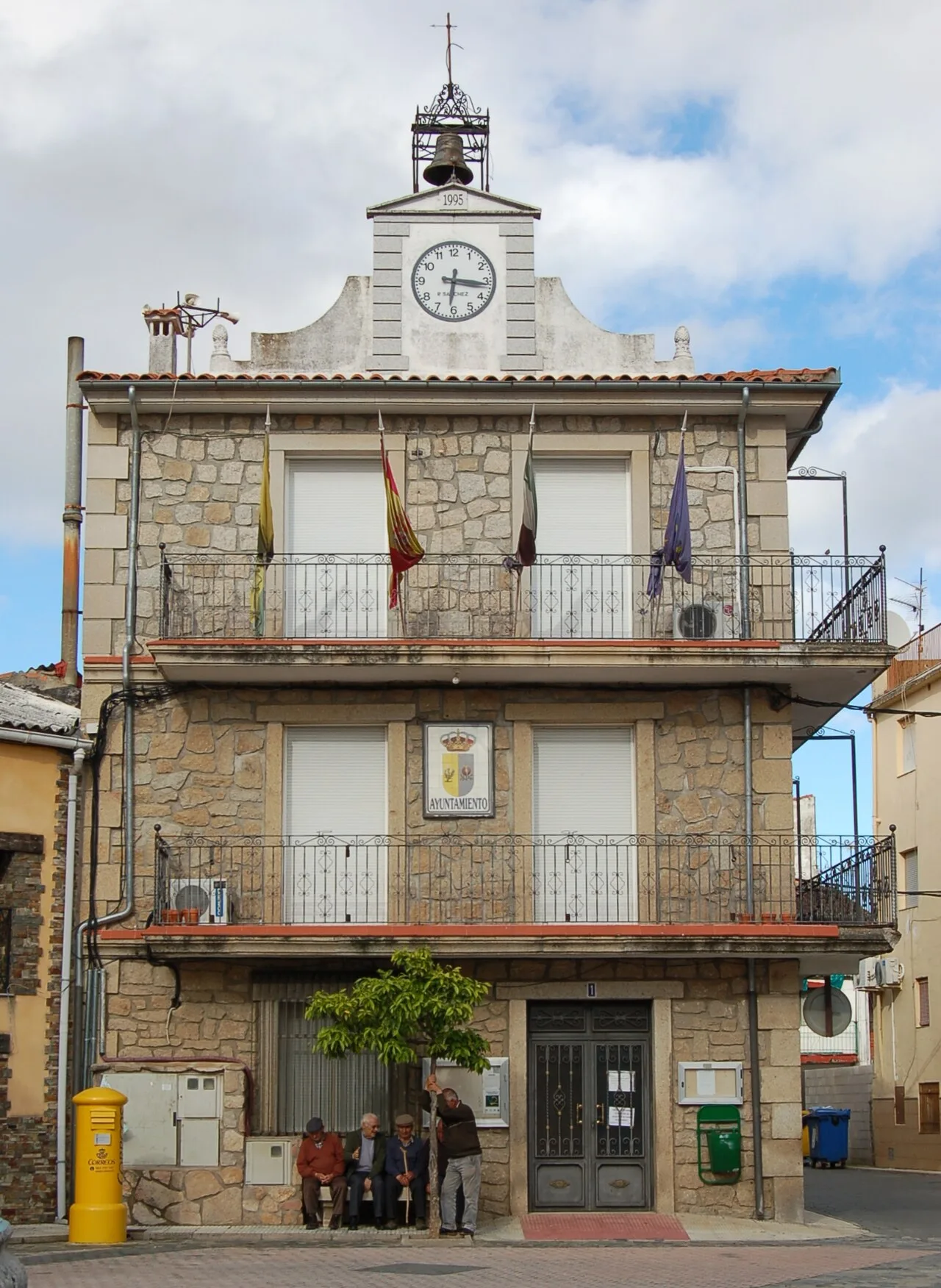Edificio de piedra con reloj y banderas en la fachada.