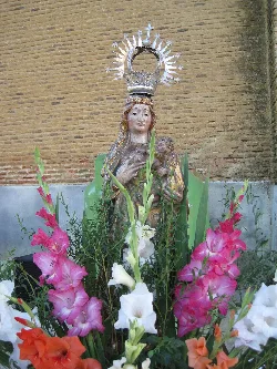 Statue of the Virgin with crown and halo, surrounded by pink, white, and orange flowers.