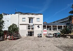 White building with windows and a symbol on the facade, cars parked in front.