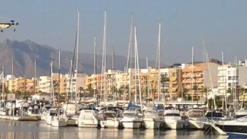 Barcos en el puerto de Garrucha con edificios y montañas al fondo.
