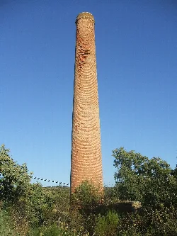 Una torre de ladrillo alto en un paisaje rural con árboles y cielo azul.
