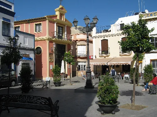 Plazoleta San Francisco con árboles, bancos y edificios coloridos en Isla Cristina.
