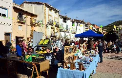 Puente de puestos y gente en la feria de Casas Bajas con edificios y montañas de fondo.