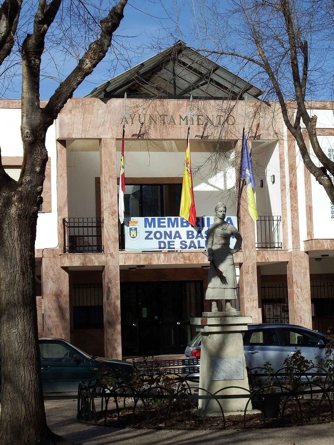 Rathaus von Membrilla mit Flaggen und einer Statue auf dem Platz.