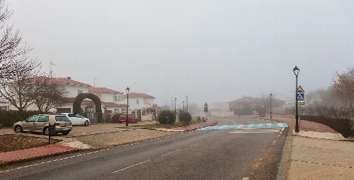 Street with houses, cars, and street lamps in Fuentenovilla on a cloudy day.