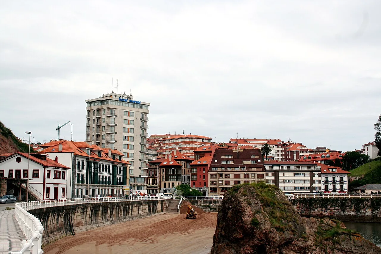 Gebäude und Strand in Candás, Asturien, mit einer felsigen Landzunge im Vordergrund.