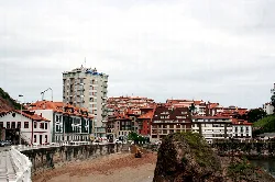 Edificios y playa en Candás, Asturias, con un promontorio rocoso en primer plano.