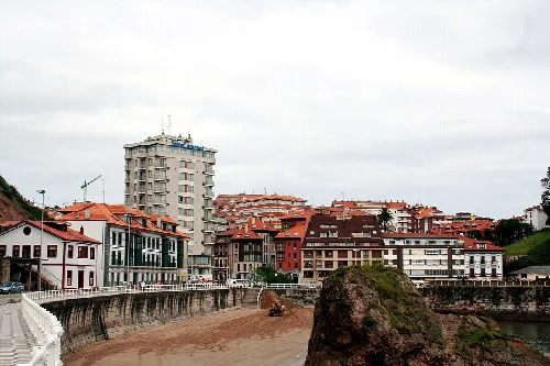 Edificios y playa en Candás, Asturias, con un promontorio rocoso en primer plano.