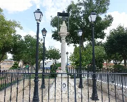 Estatua de la Virgen de la Piedad en un monumento rodeado de farolas y árboles.