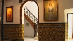 Sala del museo con pinturas en las paredes y escaleras de madera tallada.