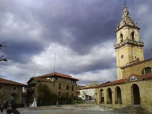 Plaza con iglesia y edificios en Iurreta, Vizcaya, bajo cielo nublado.