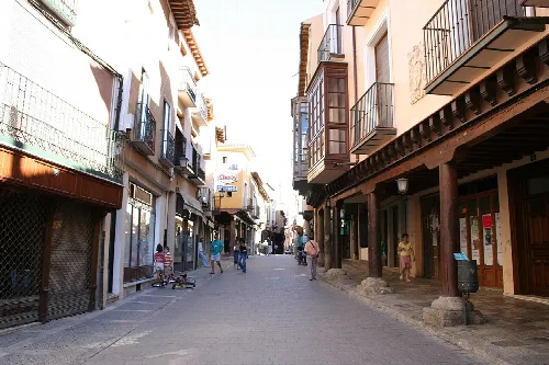 Calle con soportales, tiendas y personas en Medina de Rioseco.