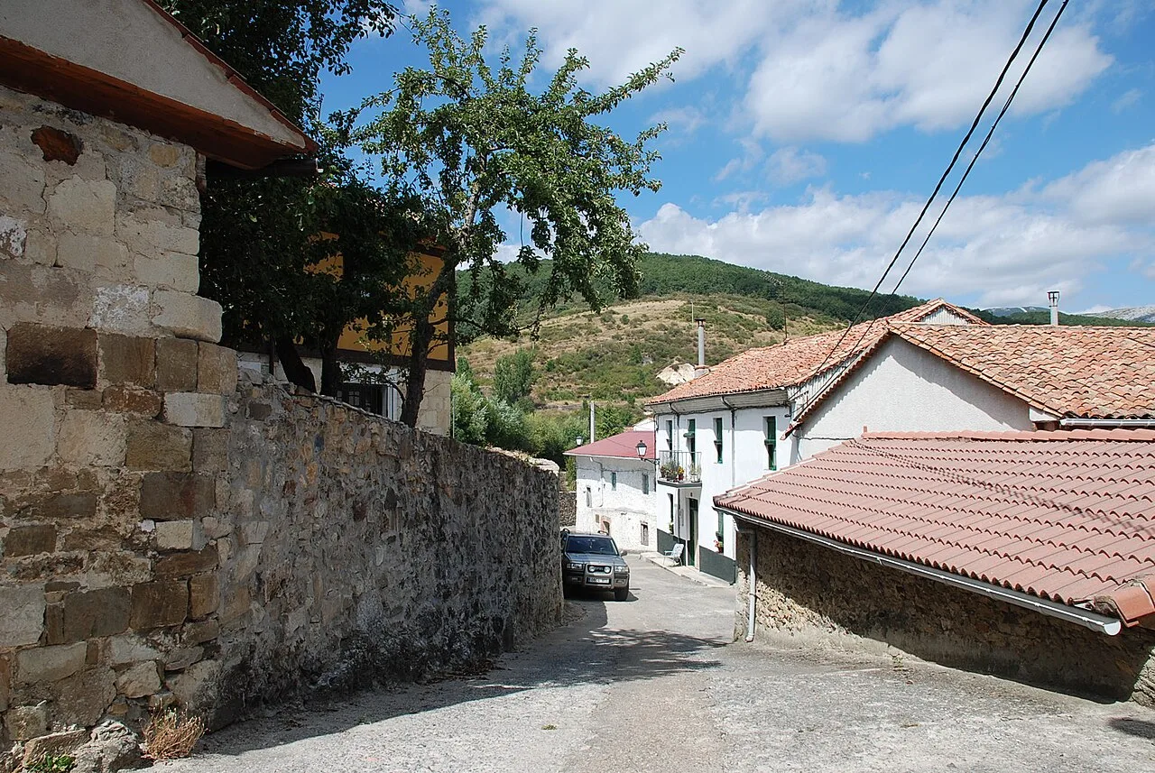 Calle estrecha con casas tradicionales y colinas verdes en el fondo.