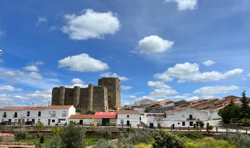 Mittelalterliches Schloss in Villagarcía de la Torre mit weißen Häusern und blauem Himmel mit Wolken.